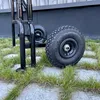 A close-up view of the wheels and frame of a black hand truck on a paved surface with grass growing between the stones. Anteprima dell’immagine prodotto