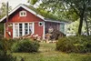 A man is chopping wood in front of a red cabin with a green roof. Produktbild-Vorschau