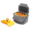 A grey compost bin filled with vegetable scraps, with carrots and potatoes in front of it. Voir les images du produit