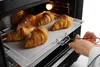 A person is taking a baking tray with croissants out of an oven. Produktbild-Vorschau
