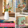 A collage of images showing a building block flower bouquet in a vase, a wrapped bouquet, and its packaging. Produktbild-Vorschau