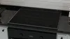A close-up view of a black glass stovetop cover on a kitchen counter. Podgląd zdjęcia produktu