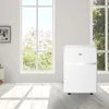 A white portable air conditioner is placed in a bright room with large windows. Produktbild-Vorschau