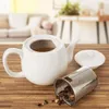 A white ceramic teapot with a removable infuser and lid sits on a wooden table, with a blurred living room in the background. Podgląd zdjęcia produktu