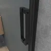 A close-up view of a black shower door handle against a gray wall. Produktbild-Vorschau