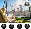 A woman is reading a book while children are jumping on a trampoline in the background. Produktbild-Vorschau