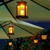 Several solar-powered lanterns with LED candles are hanging from an outdoor umbrella and foliage. Voir les images du produit