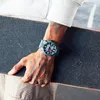 A person holding a skateboard, wearing a watch. Produktbild-Vorschau
