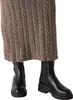 A close-up shot of a person's legs wearing a brown cable-knit skirt and black Chelsea boots. Anteprima dell’immagine prodotto