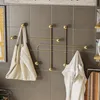 A gold metal wall hook with a minimalist design, featuring several hooks and ball-shaped accents. A beige tote bag is hung on the left hook, and a white towel is draped over a hook on the right. The hooks are mounted on a gray tiled wall. Voir les images du produit
