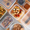 A top-down view of several clear plastic food storage containers filled with various snacks and cookies, arranged on a wooden surface. Produktbild-Vorschau