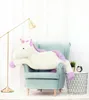 A large plush unicorn is lying on a light blue armchair in a room with white curtains. Anteprima dell’immagine prodotto