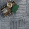 A tray with a candle, a small vase with dried flowers, and a green book sits on a gray textured rug. Produktbild-Vorschau