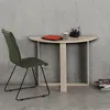 A green chair is placed next to a light wood desk with a laptop, mug, and pens on it, against a concrete wall. Náhľad obrázku produktu