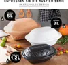 Three Römertopf clay pots of different sizes and colors (beige, white, black) are displayed on a wooden table with some ingredients like garlic, limes, and tomatoes. Produktbild-Vorschau