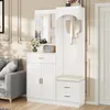 A white entryway storage unit with a mirror, coat hooks, a bench, and drawers, placed in a room with a sofa and decorative wall molding. Podgląd zdjęcia produktu