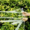 Hands holding a clear plastic tarp in front of a green leafy bush. Produktbild-Vorschau