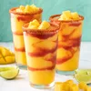 Three glasses of mango smoothie with chili rim and mango chunks on top, served with lime wedges and mango slices. Podgląd zdjęcia produktu
