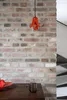Pendelleuchte Gable in Orange hängend an schwarzem Kabel vor Backsteinwand, Gesamtansicht. Produktbild-Vorschau