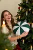 A woman is holding a round cushion with a green and white pattern in front of a decorated Christmas tree. Podgląd zdjęcia produktu