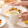 A person's hands are shown reaching for a plate of food and holding a mug of tea with lemon, set on a table with other plates and a candle. Náhled obrázku produktu