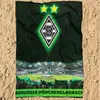A football club blanket is laid out on a sandy surface, with a stadium scene and fans depicted on the lower half. Produktbild-Vorschau