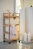 A wooden laundry cart with three fabric bins is shown in a room with a mirror and candles. Podgląd zdjęcia produktu