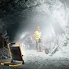 A construction worker in a mine pushing a wheelbarrow, with a work light in the foreground. Voir les images du produit