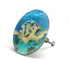 A close-up of a bathtub drain stopper featuring a sea turtle image, set against a white background. Produktbild-Vorschau
