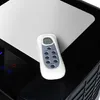 A remote control rests on the top surface of a black and white appliance. Produktbild-Vorschau