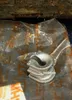 A metal part inside a plastic bag, with some text visible on the bag. Produktbild-Vorschau