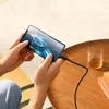 A person is holding a smartphone while it is charging, playing a game. Anteprima dell’immagine prodotto