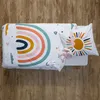 A top-down view of a children's bedding set with a rainbow and sun pattern, laid out on a wooden floor. A small stuffed bunny is placed on the pillow. Produktbild-Vorschau