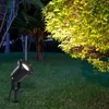 A black LED garden spotlight with an earth spike is positioned on a grassy lawn, illuminating a lush green bush with warm white light. Anteprima dell’immagine prodotto