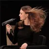 A woman is using a hairdryer on her hair, which is blowing in the wind. Podgląd zdjęcia produktu