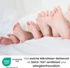 Several pairs of feet of different sizes are resting on a white bed. Produktbild-Vorschau