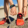 A person tying their shoelaces on a pair of orange running shoes, wearing a blue fitness tracker on their wrist. Produktbild-Vorschau