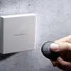 A hand holding a black transponder near a white SimonsVoss device mounted on a concrete wall. Produktbild-Vorschau
