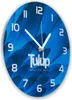 A round blue clock with white numbers and hands, featuring a floral pattern and brand name. Produktbild-Vorschau