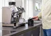 A person is using an espresso machine and a knock box in a kitchen setting. Náhled obrázku produktu