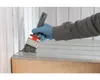A person wearing blue gloves is painting a wooden surface with a paintbrush. Produktbild-Vorschau