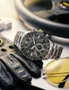 A watch, gloves, and sunglasses are arranged on a metallic surface, with a steering wheel in the background. Anteprima dell’immagine prodotto