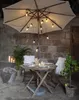 An outdoor dining set with a patio umbrella decorated with string lights. Podgląd zdjęcia produktu