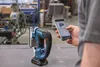 A person is holding a smartphone and looking at it, with a cordless jigsaw in the foreground. Anteprima dell’immagine prodotto
