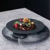 A dessert is presented on a dark plate, which is elevated by two stones over a larger plate with smoke effects. Voir les images du produit
