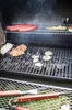 A barbecue grill with food cooking on it, including hot dogs, meat, and vegetables. Barbecue tools are visible in the foreground. Podgląd zdjęcia produktu