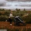 A woman is running with a stroller in a natural outdoor setting. Produktbild-Vorschau