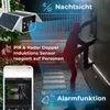 A security camera with solar panels is shown detecting a person climbing a wall at night, with a smartphone displaying the camera feed. Produktbild-Vorschau