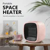 A pink portable space heater is shown on a wooden table next to a pink teacup. The background is a light gray wall with a plant. Produktbild-Vorschau