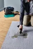 A person is using a portable carpet cleaner on a rug, with the cleaner unit in the background. Produktbild-Vorschau